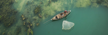 Person in a traditional fishing boat next to a green barrier reef.