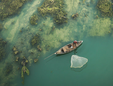 Person in a traditional fishing boat next to a green barrier reef.