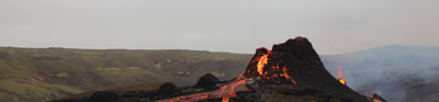  A volcano slips glowing red, yellow and black glowing lava onto a progressivly charred hilly grassland