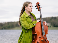 Sarah Smout standing with her cello, with a lake in the background