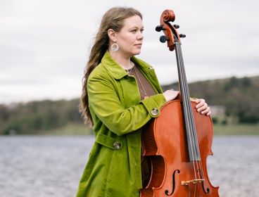 Sarah Smout standing with her cello, with a lake in the background