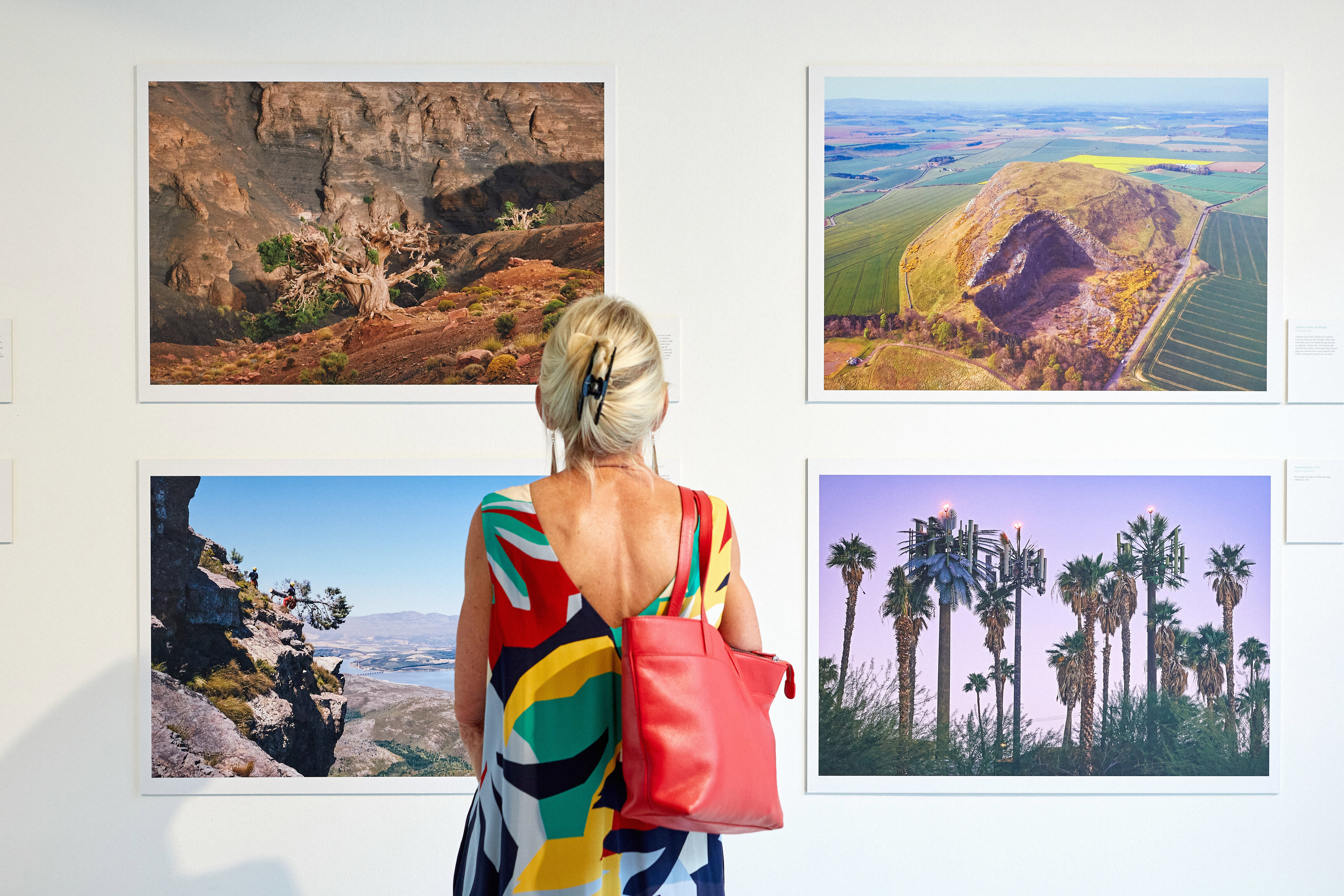 A woman wearing a colourful dress standing in front of four landscape photographs in an exhibition