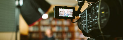 A person sitting in front of a bookcase and a camera set up for an interview.