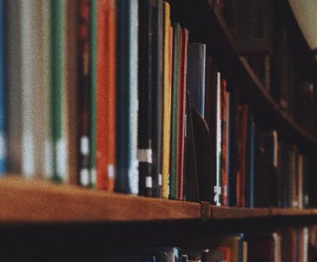 Books stacked on a wooden shelf.