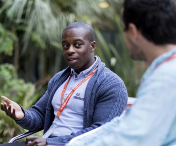 Two people having a conversation. One person on the right is sitting with their back to the camera and is blurred out.