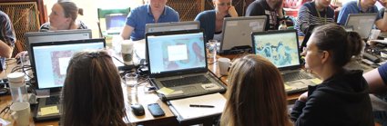 People sat around a table working on laptops with mapping software open. 