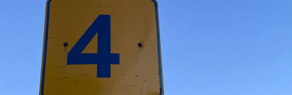 A yellow and black sign showing the number 4 on a blue sky background.