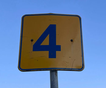 A yellow and black sign showing the number 4 on a blue sky background.