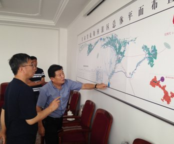 Three people looking and pointing at a large map pinned to a wall. 