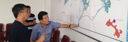 Three people looking and pointing at a large map pinned to a wall.