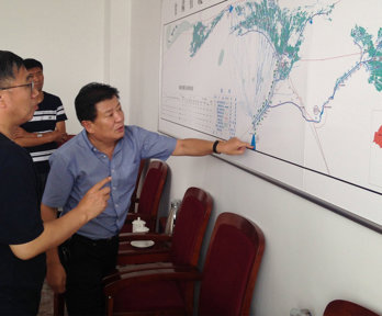 Three people looking and pointing at a large map pinned to a wall.