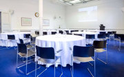 Caberet style tables and chairs facing a projector at the front of a brightly lit room.