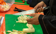 Close up of a person's hand. The person is cutting vegetables with a large kitchen knife.