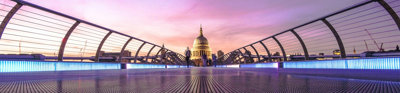 Millennium Bridge with St Paul's cathedral at the end of the bridge. The sky is in various hues of orange, pink and purple.