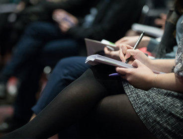 Woman holding a pen and notebook while attending a lecture..