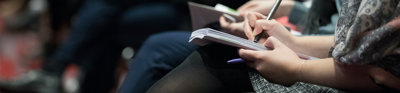 Woman holding a pen and notebook while attending a lecture..