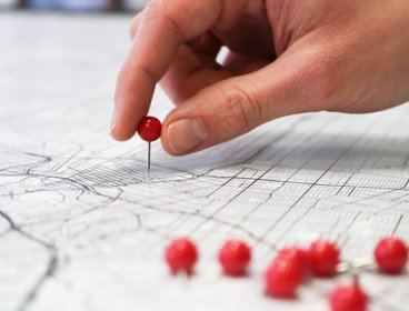 Person holding a round red pin and placing it on a map