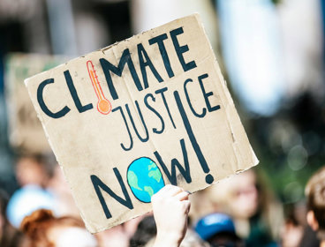 Hand holding up 'climate justice' sign among group of people.