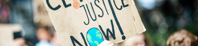 Hand holding up 'climate justice' sign among group of people.