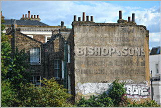 A residential building with old, faded painting on the side saying 'Bishop and Sons', suggesting that the building was a retail premises or factory previously