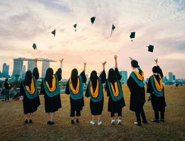 Students at graduation throwing graduation caps into the the year against backdrop of Singapore.