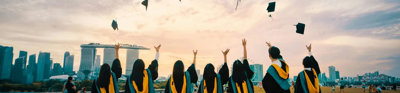 Students at graduation throwing graduation caps into the the year against backdrop of Singapore.