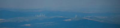 A landscape in hues of blue with groups of wind turbines on hills in the distance.