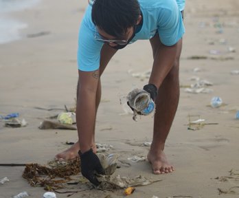 Person bending over to pick up litter on a beach.