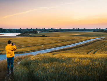 A person is taking a picture of a road which cuts through a field.