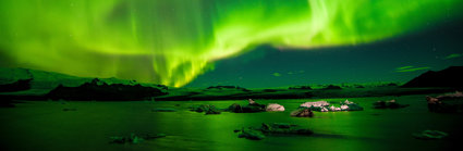 The northern lights shiining brihght green and yellow over a rocky landscape next to the sea