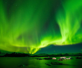 The northern lights shiining brihght green and yellow over a rocky landscape next to the sea