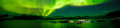 The northern lights shiining brihght green and yellow over a rocky landscape next to the sea
