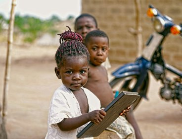 Girl holding a book near other children and a motorcycle