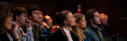 A white blond woman looks at the stage while surrounded by a small group of audience members of mixed genders sitting in the Society's lecture theatre.