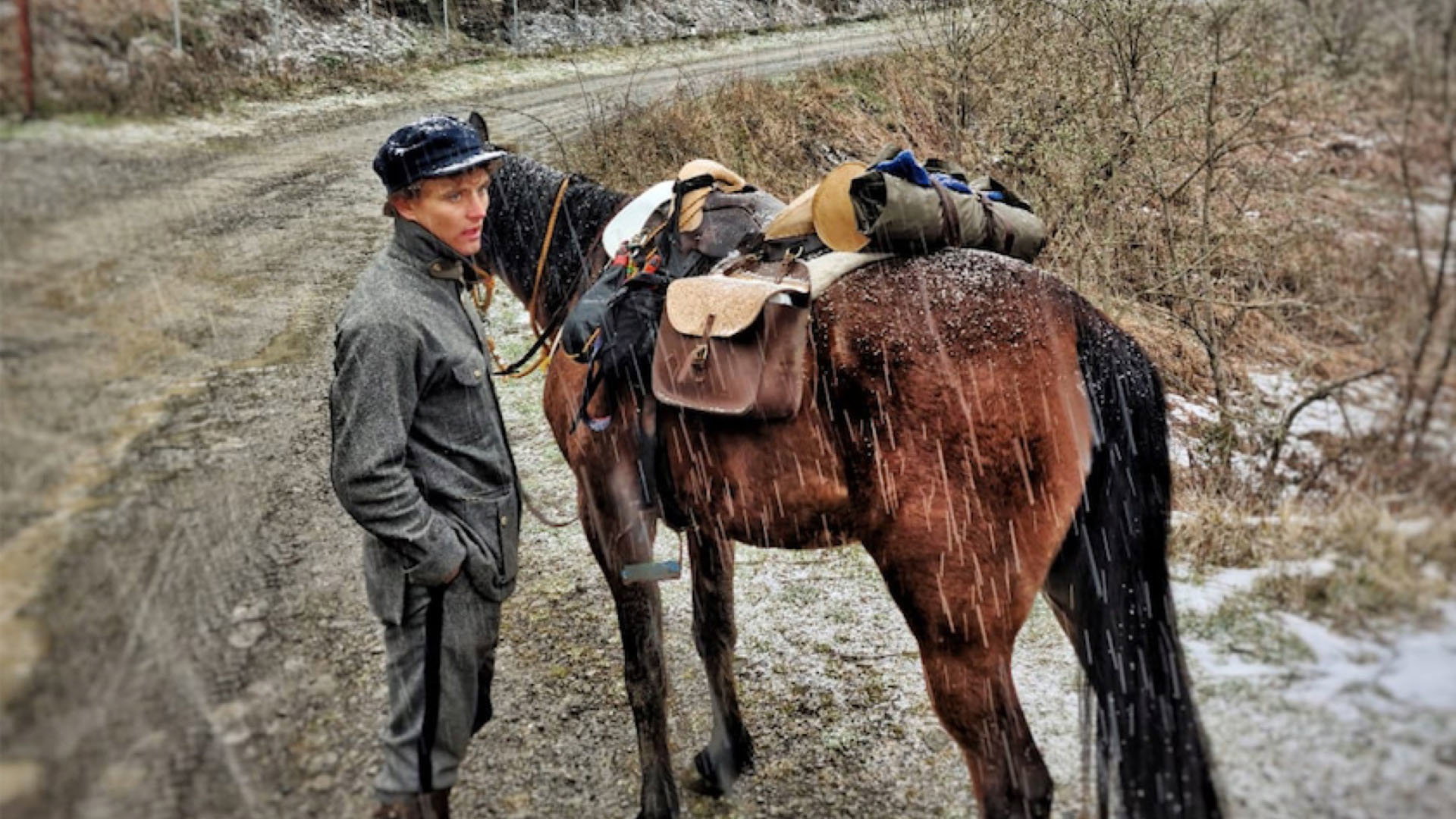 Person standing next to a horse in the rain, on a muddy track.