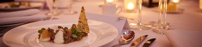 A formal dinner table with food, cutlery, wine glasses and glass candleholders with lit tealights.