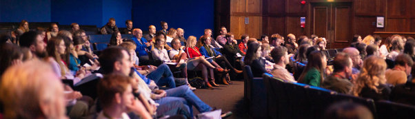 Large group of people sat in a lecture hall attending a presentation. 