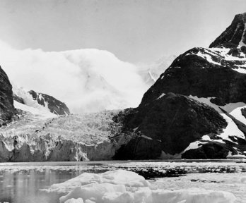 Black and white photograph showing a landscape with ice, snow and mountains.