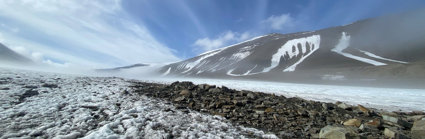 Low-angle shot of a windswept glacier with rocky surface and clear blue sky.
