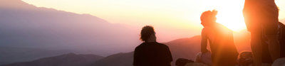 Two people sitting and one person standing near cliff taken during golden hour.