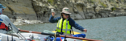 A person wearing a life jacket in a rubber boat taking measurements from a river.