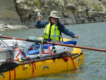 A person wearing a life jacket in a rubber boat taking measurements from a river.