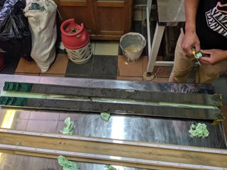 Two sediment sample cores lain on a lab table next to a measuring tape. A researcher is stood next to the table. 