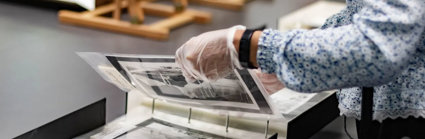 A researcher wearing archival gloves viewing historic photographs in a folder.