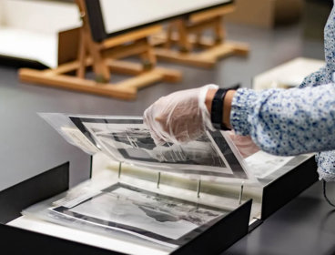 A researcher wearing archival gloves viewing historic photographs in a folder.