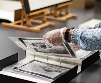 A researcher wearing archival gloves viewing historic photographs in a folder.