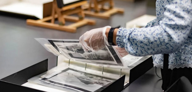 A researcher wearing archival gloves viewing historic photographs in a folder.