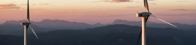 two wind turbines with mountain view at sunset