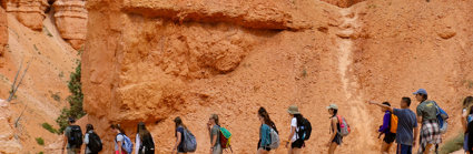 A group of students walking in a line through a red sandstone environment, with rocky outcrops and small bushy green plants 