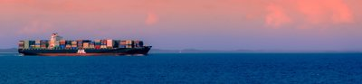 A cargo ship on the ocean with a pink sky